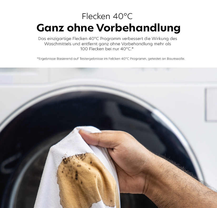 Feature-Banner, Ein Hand hält ein weißes Tuch mit braunen Flecken, während eine Waschmaschine im Hintergrund sichtbar ist. Text: 'Flecken 40° C Ganz ohne Vorbehandlung'