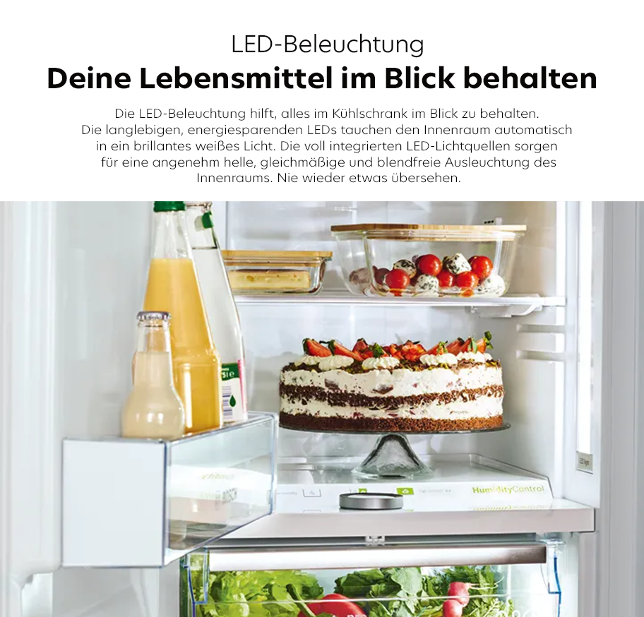 Feature-Banner, Innenraum eines Kühlschranks mit LED-Beleuchtung, gefüllt mit Flaschen, einer Torte auf einem Glasständer, einer Schale mit Tomaten und Eiern sowie frischem Gemüse in der unteren Schublade.'