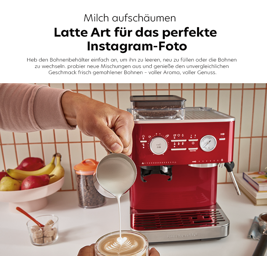Feature-Banner, Kitchenaid Milchaufschäumer in Rot, Person gießt Milch in eine Tasse mit Latte Art, Espressomaschine im Hintergrund, sichtbare Bedienelemente.'