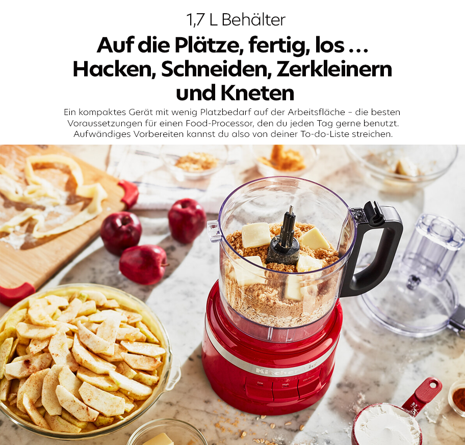 Feature-Banner, Roter Food-Processor mit 1,7-Liter-Behälter auf Marmorarbeitsfläche, umgeben von Apfelscheiben, Kirschen und Messbechern mit Zutaten.'