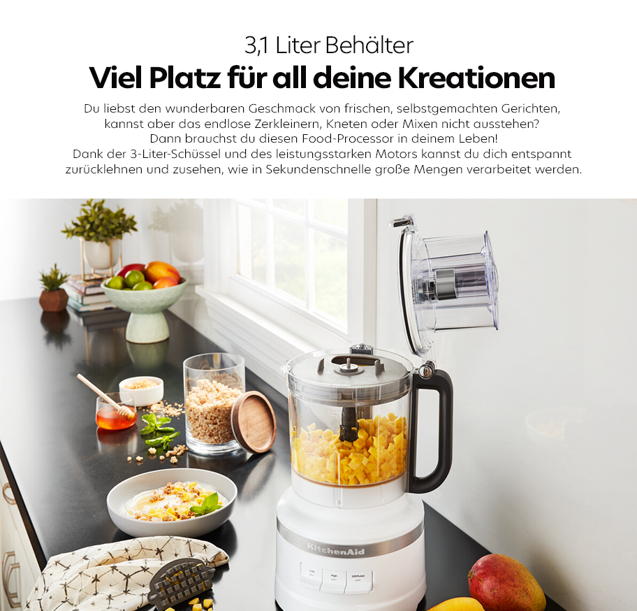 Feature-Banner, Küchenarbeitsplatte mit weißem KitchenAid Food-Processor, 3,1-Liter-Behälter gefüllt mit geschnittenem Obst, daneben Schüssel mit Müsli, Obstschale und Gewürzgläser.'