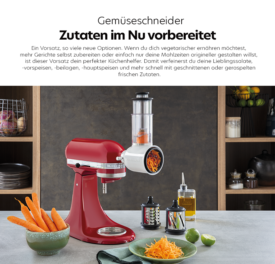 Feature-Banner, Küchenmaschine von KitchenAid in Rot mit Gemüseschneider-Aufsatz, der Karotten in Streifen schneidet. Im Hintergrund sind frisches Gemüse und Küchenutensilien sichtbar'.