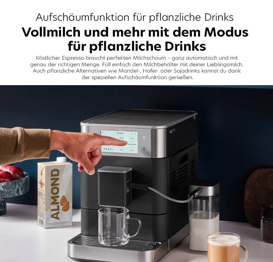 Feature-Banner, Kaffeevollautomat von KitchenAid mit Aufschäumfunktion für pflanzliche Drinks. Hand greift nach dem Bedienfeld. Sichtbare Tassen mit pflanzlicher Milch.'.