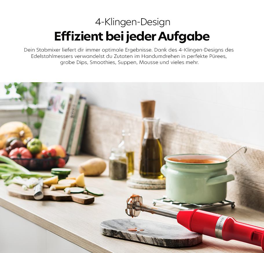 Feature-Banner, Stabmixer mit rotem Griff und 4-Klingen-Design liegt auf Marmorplatte in moderner Küche mit Gemüse, Ölflaschen und Kochtopf im Hintergrund.'