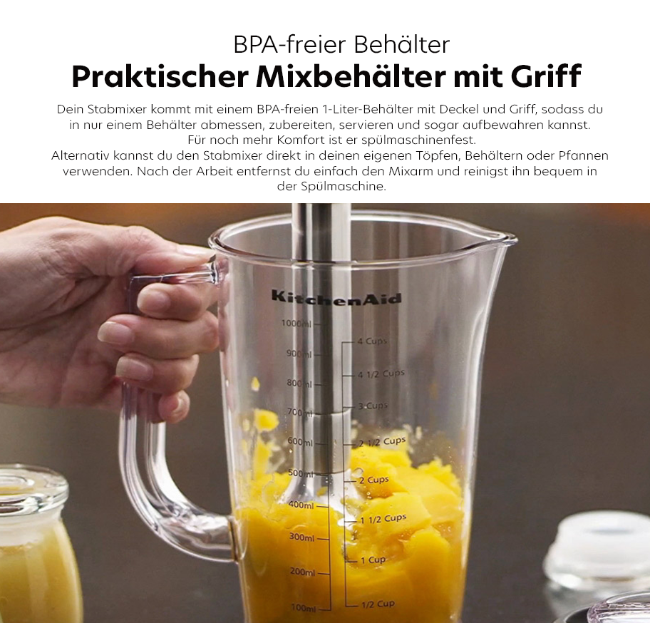 Feature-Banner, Hand hält transparenten KitchenAid-Mixbehälter mit Griff, Messskala und gelbem Inhalt, auf Holzuntergrund, daneben Gläser mit Zutaten.'
