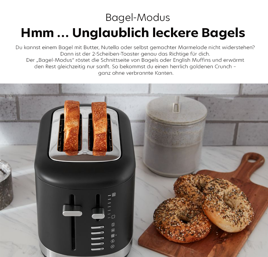 Feature-Banner, Schwarzer 2-Scheiben-Toaster mit zwei gerösteten Brotscheiben, daneben drei mit Körnern bestreute Bagels auf Holzbrett und Keramikgefäß auf Marmorarbeitsplatte.'