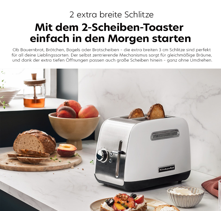 Feature-Banner, KüchenAid 2-Scheiben-Toaster mit tiefen, extra breiten Schlitzen auf weißer Küchenarbeitsplatte, daneben Brot, Pfirsiche und belegte Brotscheiben.'