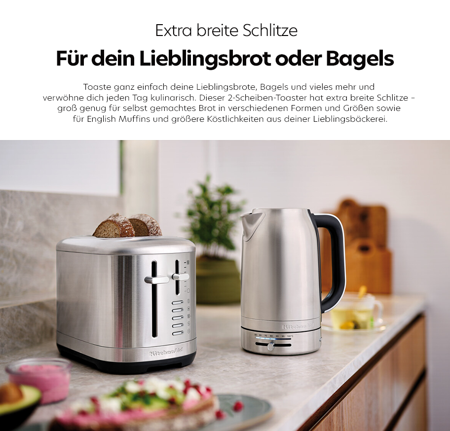 Feature-Banner, Küchenarbeitsplatte mit silbernem 2-Scheiben-Toaster mit breiten Schlitzen und silbernem Wasserkocher mit schwarzem Griff, im Hintergrund unscharfe Küchenutensilien.'