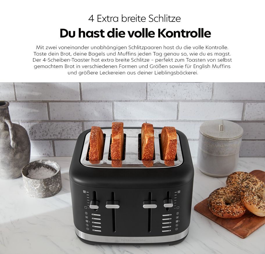 Feature-Banner, Schwarzer 4-Scheiben-Toaster mit extra breiten Schlitzen, vier Toastscheiben stecken darin, daneben Backutensilien und Bagels auf weißer Küchenarbeitsplatte.'