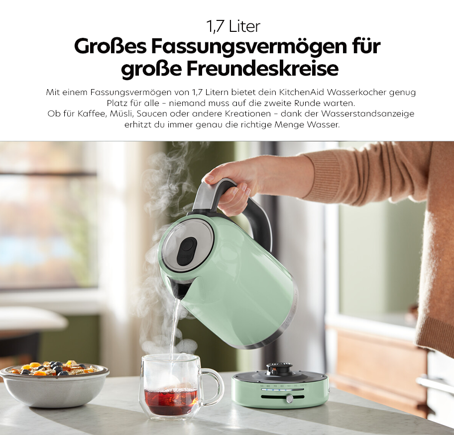 Feature-Banner,KitchenAid Wasserkocher in Pastellgrün mit 1,7 Liter Fassungsvermögen, dampfend, wird von Hand über eine Glastasse mit Tee gehalten.'