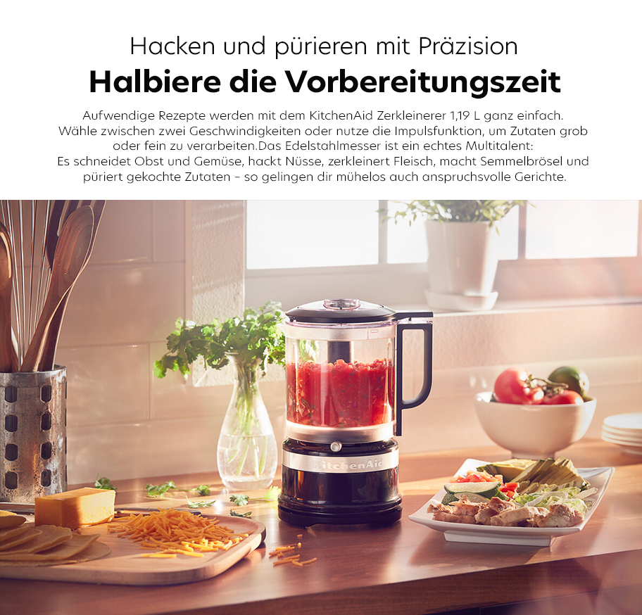 Feature-Banner, Küchenzeile mit KitchenAid Zerkleinerer 1,19 Liter gefüllt mit roten Zutaten, daneben Schneidebrett mit Käse und Nudeln, Besteckbehälter, Vase mit grünem Zweig und Teller mit belegten Broten.'