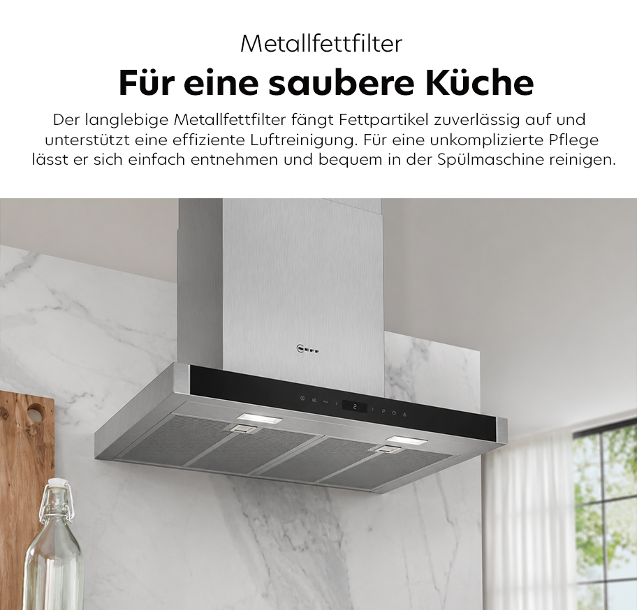 Feature-Banner, Edelstahl-Dunstabzugshaube von NEFF mit drei Metallfettfiltern und integrierter Beleuchtung an einer Küchenwand mit Marmoroptik.'